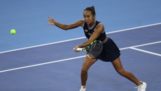 A female tennis player tennis returns a shot on a hard court with a racket in her left hand.