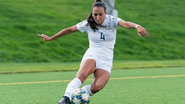 A women's soccer player kicks a ball.