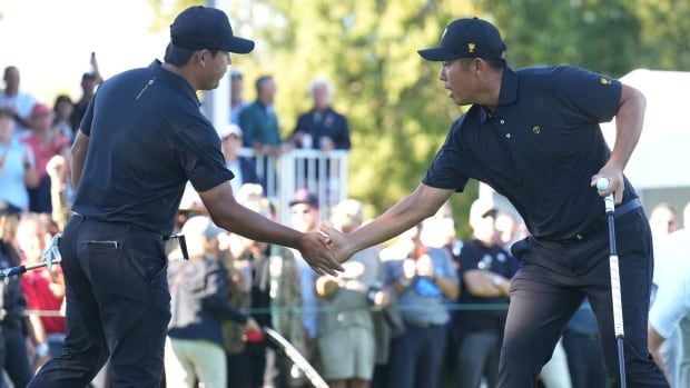 Two male golfers shake hands in celebration.