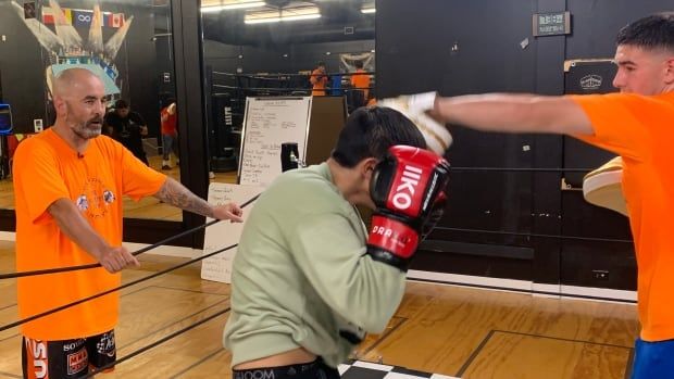 A man watches from outside a boxing ring as two young men spar inside.