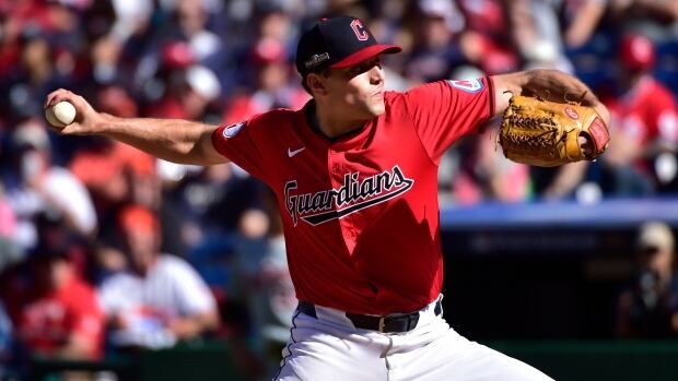 A male baseball pitcher winds up to throw a pitch with his right hand as the crowd looks on during a day game.