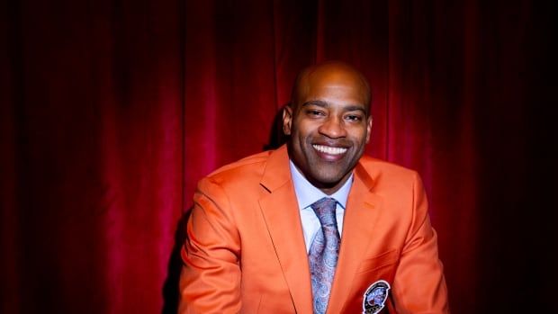 A person in a suit smiles and holds a basketball while sitting and posing for a photograph.