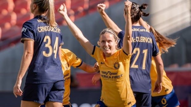 A female soccer player is seen with her hands up in celebration.