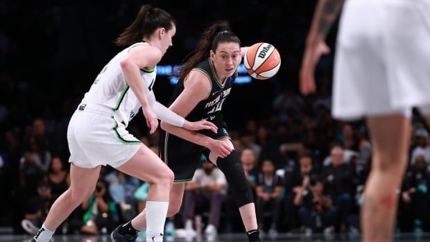 A female basketball player is seen with the ball as she's pressured by an opposition player.