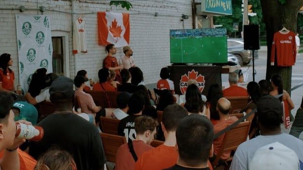 A group watches a game on a TV outside.