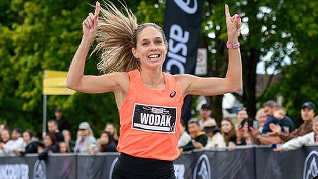 Canadian women's marathon runner Natasha Wodak raises both arms and points upward with the index finger on each hand while crossing the finish line of a race in Vancouver.