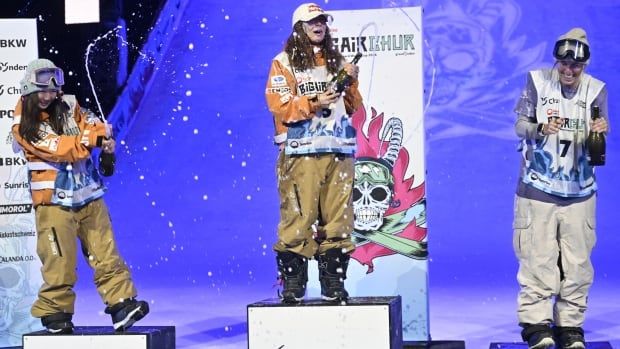 Three female snowboard athletes celebrate on the podium. 