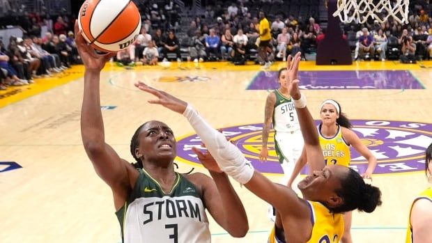 A women's basketball player attempts a layup while contested.