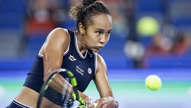 A female tennis player prepares to hit an incoming ball with both hands on her racket during a match.