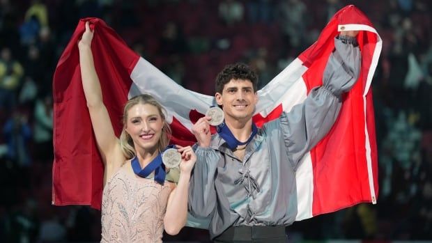 An ice dance pair pose with silver medals and a Canadian flag.