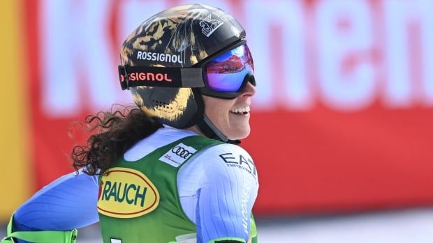 A women's skier, wearing a helmet and ski goggles, smiles after a race.