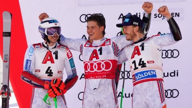 Three men's skiers raise their arms in celebration.