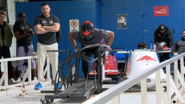 A man stands behind a bobsleigh sled on a practice track. 