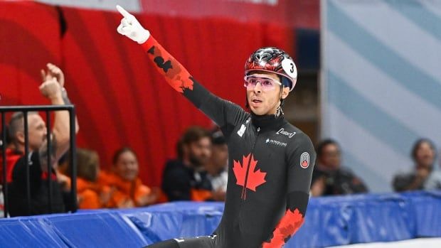 A men's speed skater points upward.