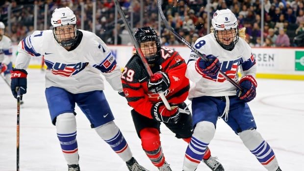 Three skaters compete for a puck during a women's hockey game.