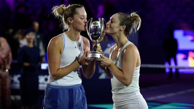 Two female tennis players are seen kissing a shinny trophy they hold.