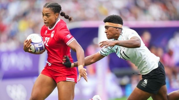 A female rugby sevens player runs past an opponent with the ball in her right arm.