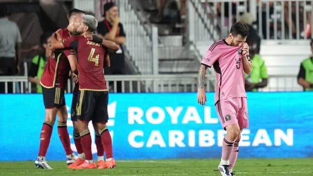 A male soccer player looks dejected as opposition players celebrate behind him.