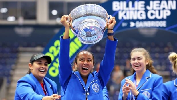 Women's tennis players celebrate while one raises a trophy.