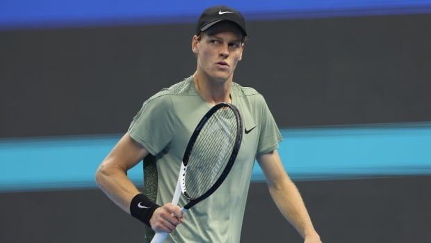 A male tennis player walks off the court while looking to his right and holding his racket in his right hand.