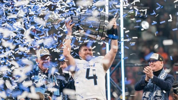 A men's football player holds up a trophy as confetti falls.