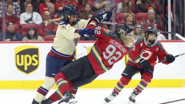 A female hockey player checks a player on the opposing team, who is mid-fall. 