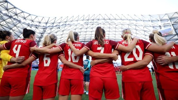 Canadian women's soccer team stand arm in arm. 