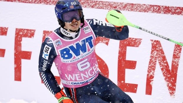 Male skier from Norway stands at bottom of ski hill reacting to his victory in a slalom race.