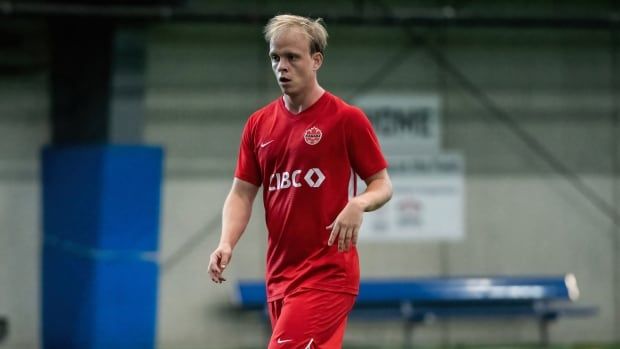 A male soccer player walking on the turf practicing.