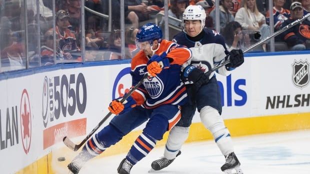 Two hockey players battle for the puck against the boards