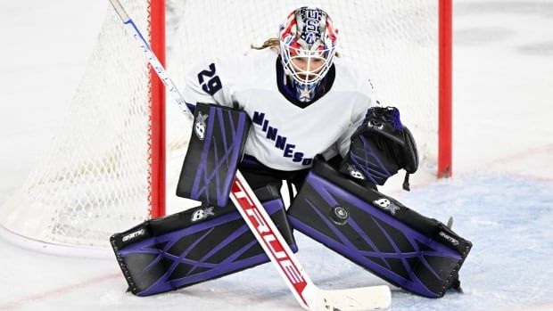 A female ice hockey goaltender wearing number 29 goes down to make a save on both knees.