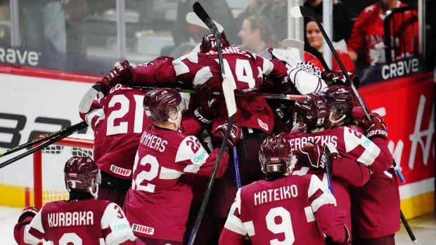 The Latvian junior team, dressed in maroon, dogpiles each other on the ice to celebrate a win at the World Junior Hockey Championship