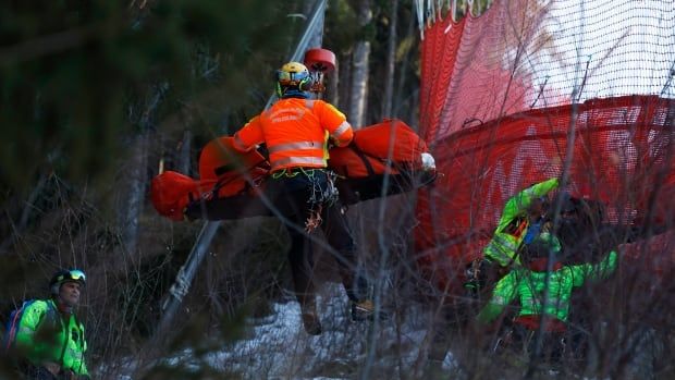 A person is airlifted away from an alpine skiing course while medical personnel assist.