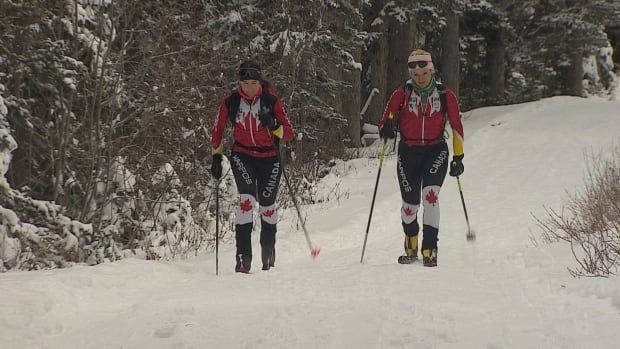 Two women wearing ski equipment glide through snow on skis.