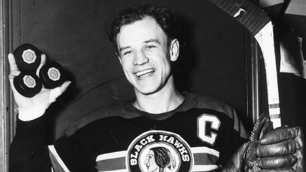 Black and white photo of a hockey player holding three pucks