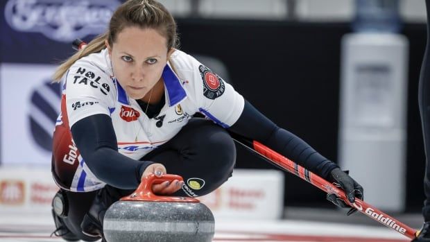 A female curling skip delivers a stone with her right hand.