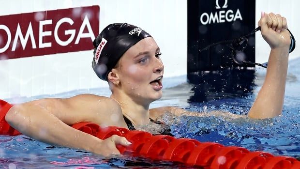 A female swimmer holds up her left hand in celebration at the end of her lane.