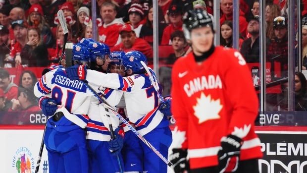 US players hug in background with a Canadian player standing in the foreground