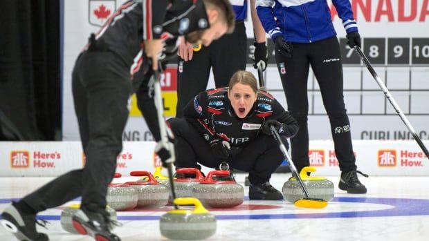 A female curling skip shouts while crouching down as her male mixed doubles partner sweeps ahead of a stone.