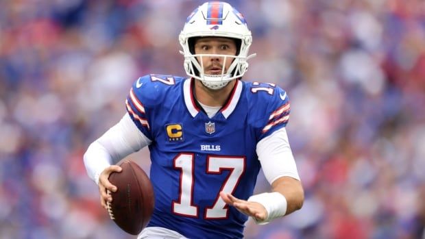 A male football quarterback wearing number 17 runs with the ball in his right hand inside a stadium filled with fans.