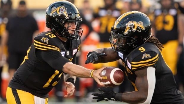 Hamilton Tiger Cats quarterback Bo Levi Mitchell (19) hands off to Hamilton Tiger Cats running back James Butler (9) during first half CFL football action against the Saskatchewan Roughriders, in Hamilton on Sunday, June 16, 2024. 