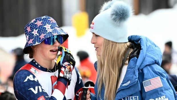 A skier wearing a bucket hat chats with a skier wearing a parka and tuque.