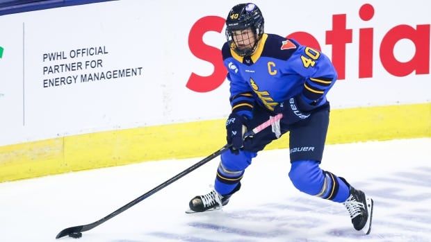 A women's hockey player stickhandles the puck next to the boards.