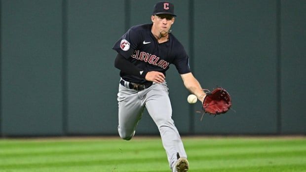 A male baseball outfielder fields a ball hit into center field.