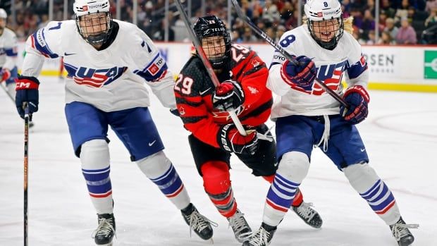 A women's hockey forward attempts to split two defenders during a game.