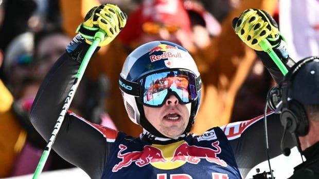 A men's alpine skier raises his arms in celebration.