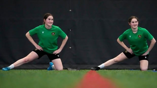 Two twin girls are pictured on a soccer field stretching.