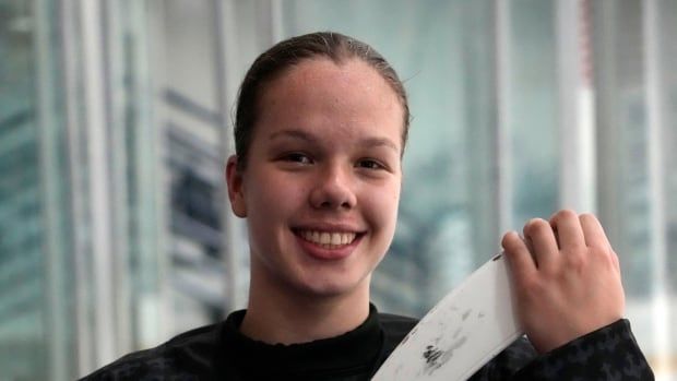 A girl holding a hockey stick smiles.