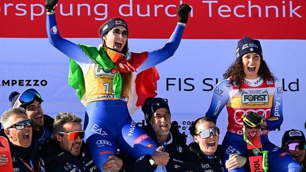 Italian women's skiers Sofia Goggia and Federica Brignone celebrate with their team on the podium of the women's downhill event at a World Cup in Cortina d'Ampezzo, Italy on January 18, 2025. 