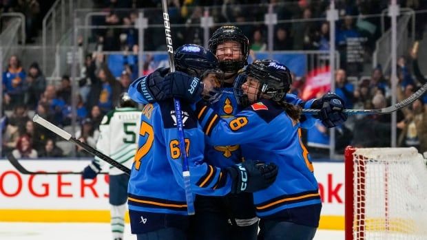 Three women's hockey teammates embrace in celebration.